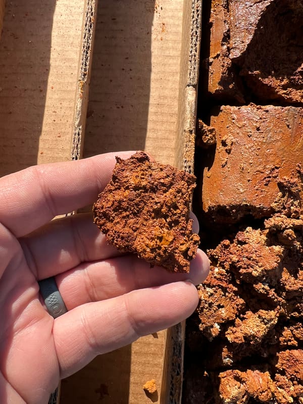 Hand holding a broken section of sanded dolomite core above the tray